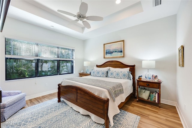 bedroom with a tray ceiling, ceiling fan, and light wood-type flooring