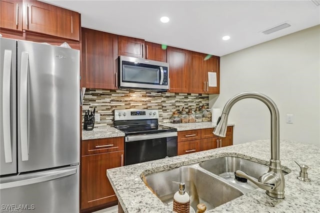 kitchen featuring light stone counters, sink, decorative backsplash, and stainless steel appliances