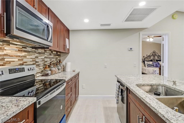 kitchen with sink, light hardwood / wood-style flooring, appliances with stainless steel finishes, backsplash, and light stone counters