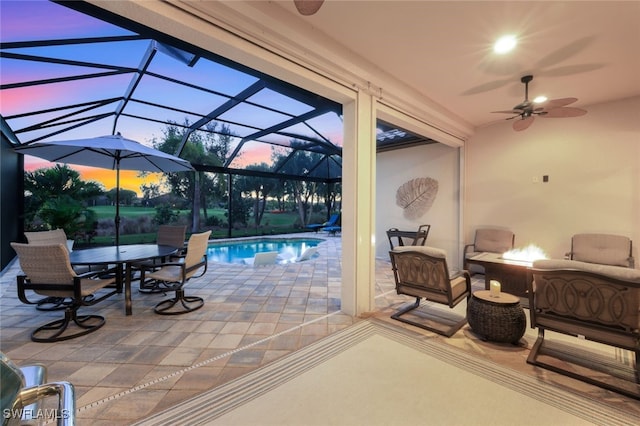 patio terrace at dusk featuring an outdoor living space, ceiling fan, and glass enclosure