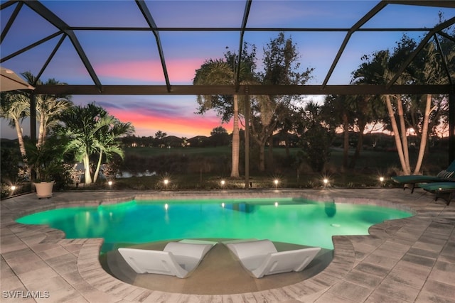 pool at dusk featuring a patio and glass enclosure