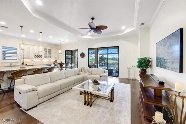 living room with dark hardwood / wood-style flooring, a tray ceiling, ornamental molding, and ceiling fan