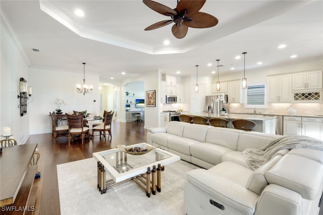 living room with a tray ceiling, ceiling fan with notable chandelier, ornamental molding, and hardwood / wood-style flooring