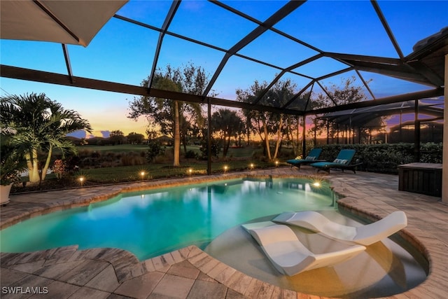 pool at dusk with glass enclosure and a patio area