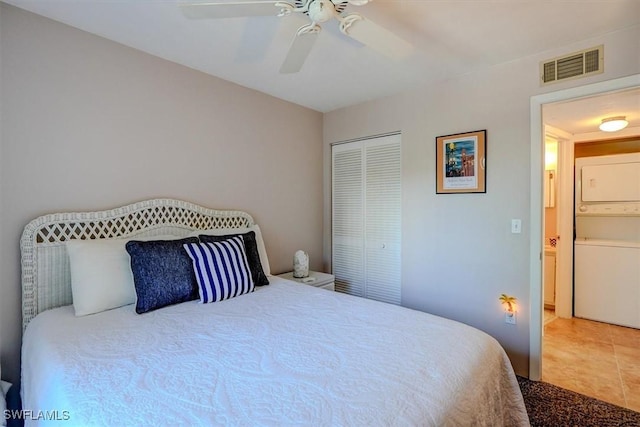 tiled bedroom with ceiling fan, stacked washing maching and dryer, and a closet