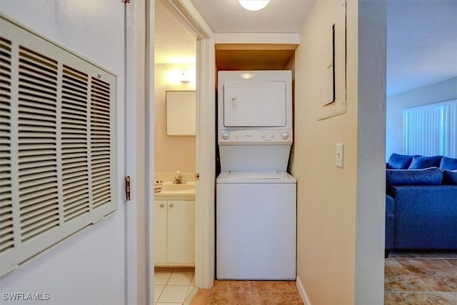 clothes washing area with sink, light tile patterned floors, and stacked washer and clothes dryer