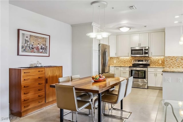 kitchen featuring white cabinetry, hanging light fixtures, stainless steel appliances, light stone countertops, and decorative backsplash