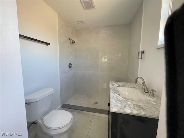 bathroom featuring tile patterned flooring, vanity, a tile shower, and toilet