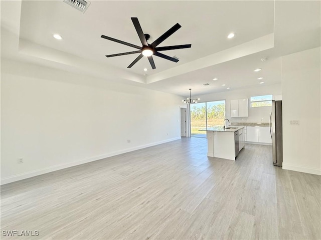 unfurnished living room with ceiling fan with notable chandelier, sink, a raised ceiling, and light hardwood / wood-style floors