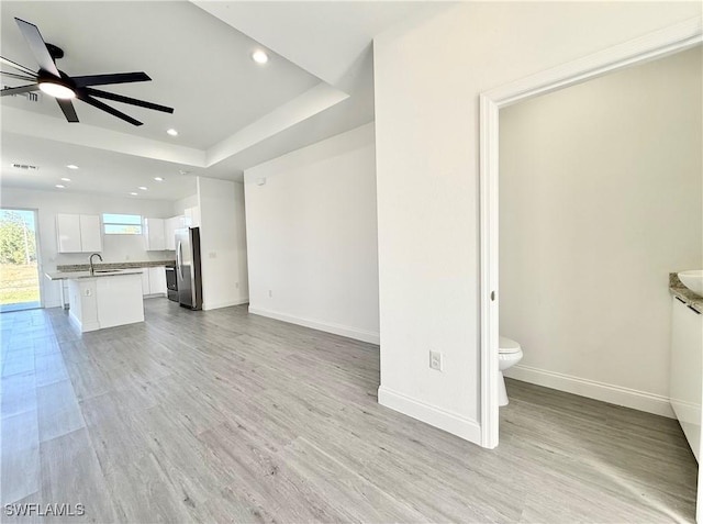 unfurnished living room featuring ceiling fan, sink, light hardwood / wood-style floors, and a tray ceiling