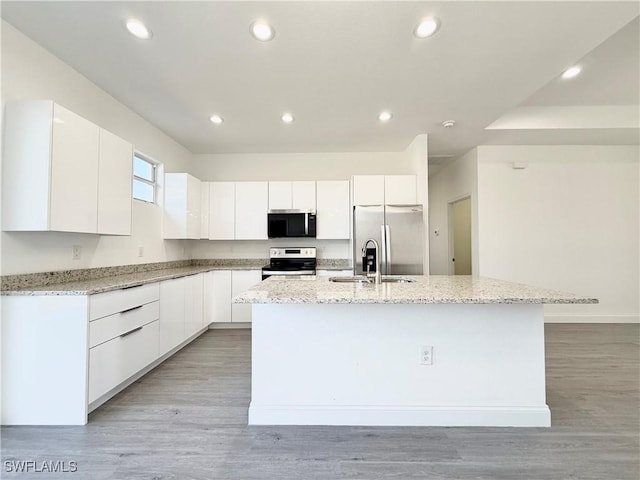 kitchen featuring light stone counters, appliances with stainless steel finishes, a kitchen island with sink, and white cabinets