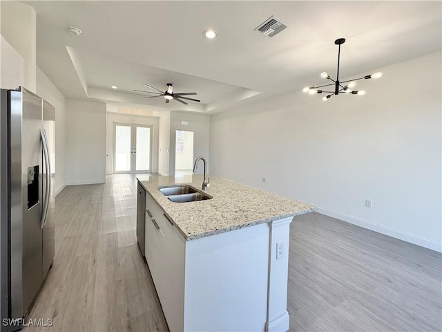 kitchen with sink, a kitchen island with sink, stainless steel refrigerator with ice dispenser, a raised ceiling, and light wood-type flooring