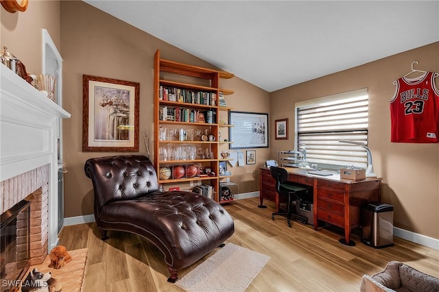 home office with a brick fireplace, vaulted ceiling, and light wood-type flooring