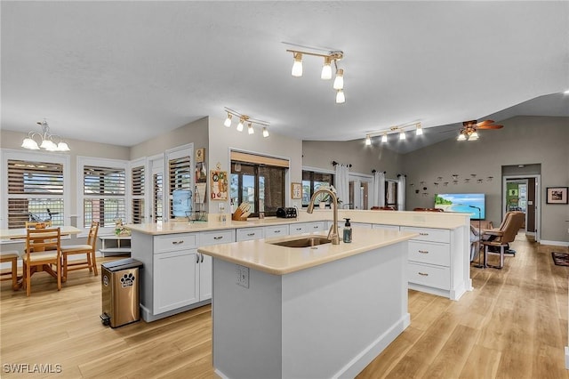 kitchen featuring vaulted ceiling, a kitchen island with sink, sink, and white cabinets