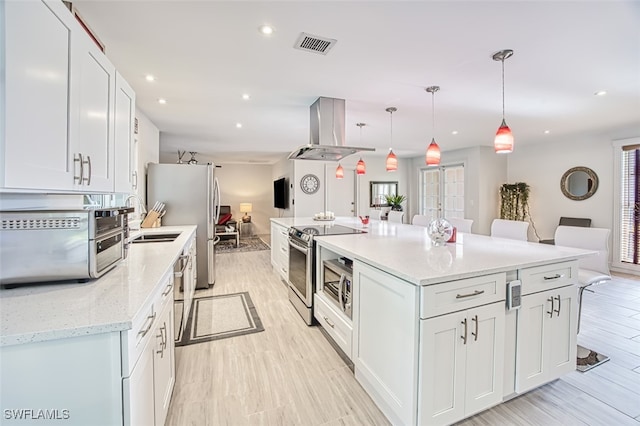 kitchen with pendant lighting, appliances with stainless steel finishes, a kitchen breakfast bar, white cabinets, and island exhaust hood