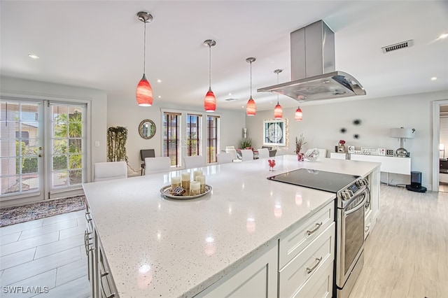 kitchen with island exhaust hood, decorative light fixtures, light stone counters, and stainless steel range with electric stovetop