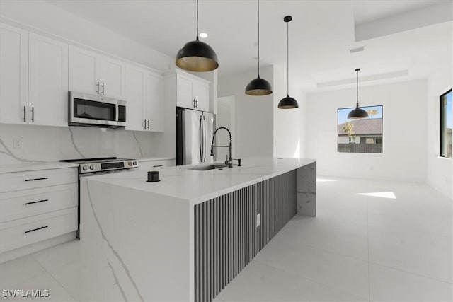 kitchen featuring light stone counters, decorative light fixtures, appliances with stainless steel finishes, a kitchen island with sink, and white cabinets