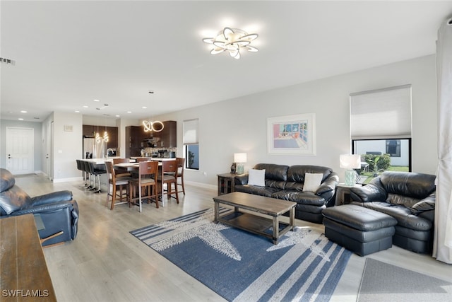 living area featuring visible vents, baseboards, a notable chandelier, and light wood-style floors