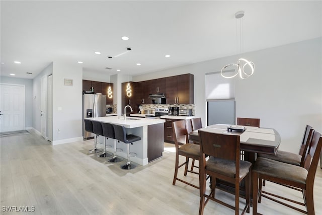 kitchen with a kitchen bar, light wood-type flooring, appliances with stainless steel finishes, a kitchen island with sink, and a sink