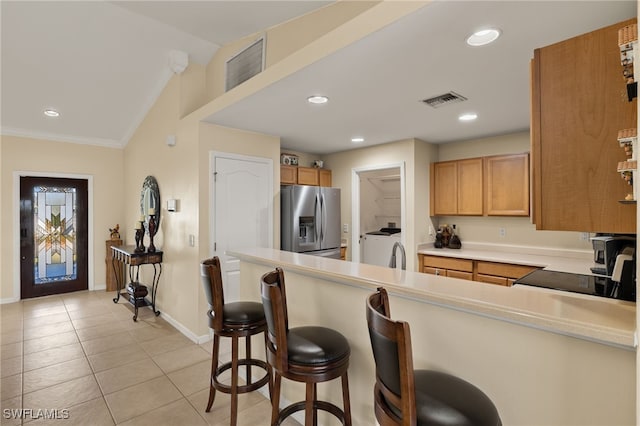 kitchen featuring stainless steel fridge, a kitchen bar, light tile patterned flooring, washer / clothes dryer, and vaulted ceiling