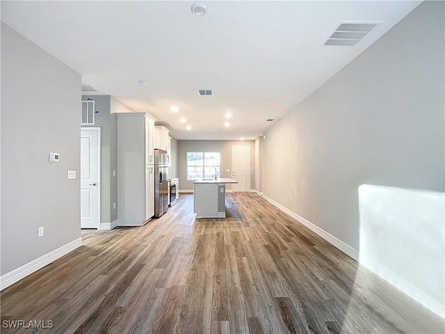 kitchen with a breakfast bar, white cabinetry, stainless steel fridge with ice dispenser, an island with sink, and hardwood / wood-style flooring