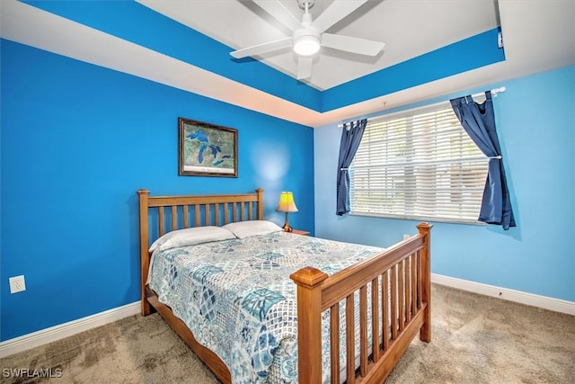 bedroom with a raised ceiling, ceiling fan, and carpet flooring