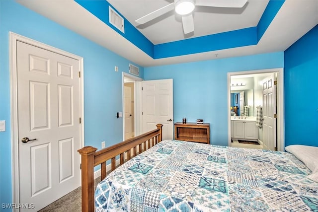 carpeted bedroom featuring a raised ceiling, ceiling fan, and ensuite bathroom