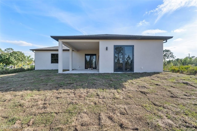 back of property featuring stucco siding, a lawn, and a patio