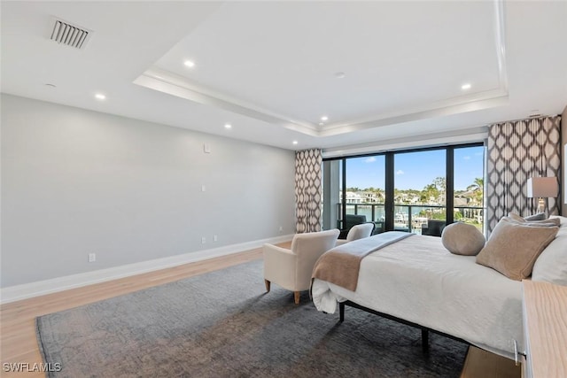 bedroom with a raised ceiling, light wood-style floors, baseboards, and visible vents