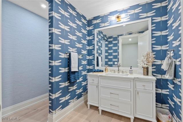 bathroom featuring wallpapered walls, vanity, baseboards, and wood finished floors