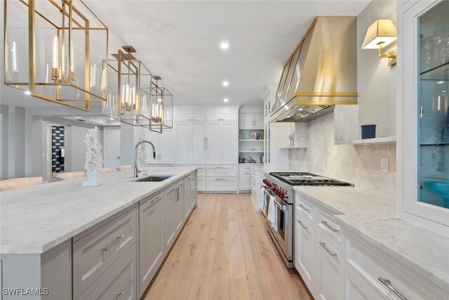 kitchen featuring white cabinets, custom exhaust hood, light wood finished floors, a sink, and range with two ovens