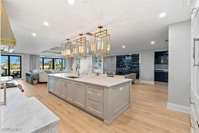 kitchen featuring open floor plan, white cabinetry, light wood-type flooring, an inviting chandelier, and a sink