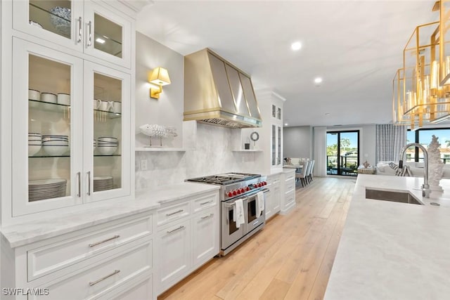 kitchen featuring backsplash, a sink, light wood-style floors, range with two ovens, and wall chimney exhaust hood