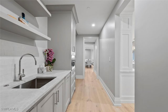 interior space featuring decorative backsplash, baseboards, a sink, open shelves, and light wood-style floors