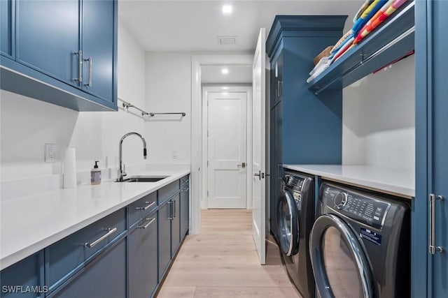 laundry room featuring light wood finished floors, washer and clothes dryer, cabinet space, and a sink