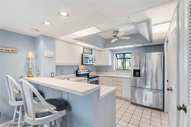 kitchen with a kitchen bar, white cabinetry, appliances with stainless steel finishes, kitchen peninsula, and a raised ceiling