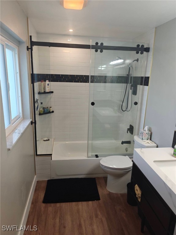 full bathroom with vanity, hardwood / wood-style floors, shower / bath combination with glass door, and toilet