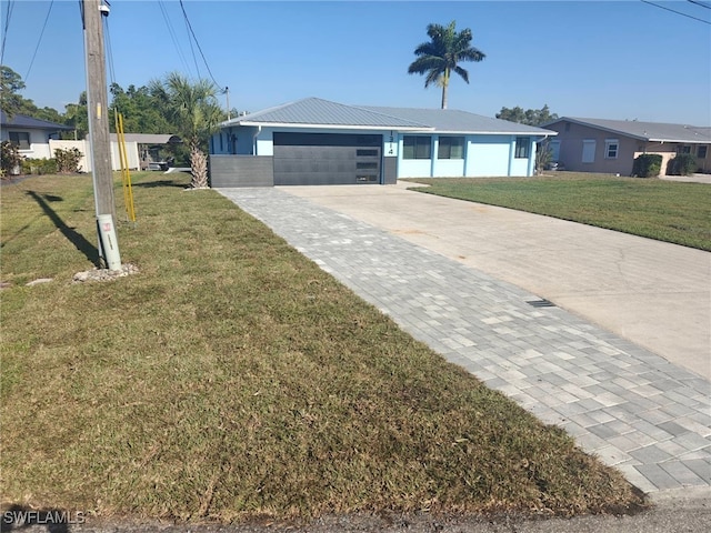 ranch-style home with a garage, metal roof, concrete driveway, and a front yard