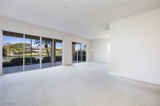 unfurnished room with carpet flooring, baseboards, and an inviting chandelier