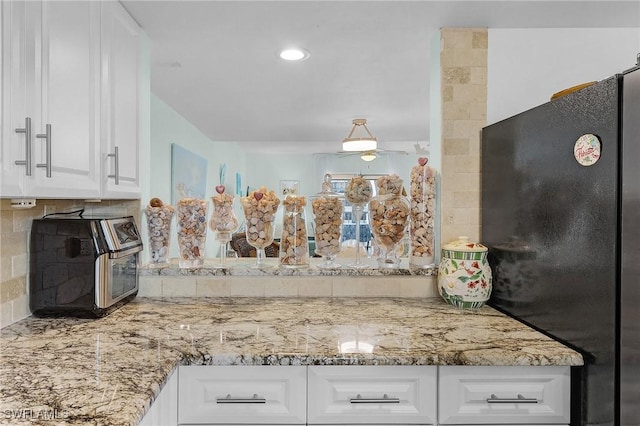 kitchen with black refrigerator, white cabinetry, light stone countertops, and decorative backsplash