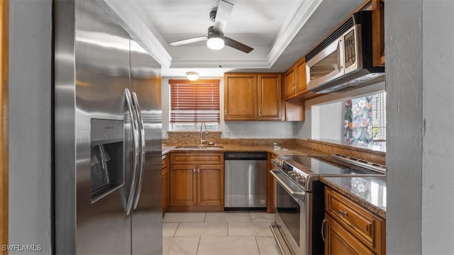 kitchen with a sink, ornamental molding, appliances with stainless steel finishes, brown cabinets, and a tray ceiling