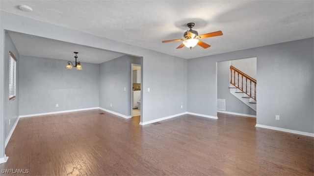 unfurnished living room featuring baseboards, visible vents, dark wood-style floors, stairway, and ceiling fan with notable chandelier