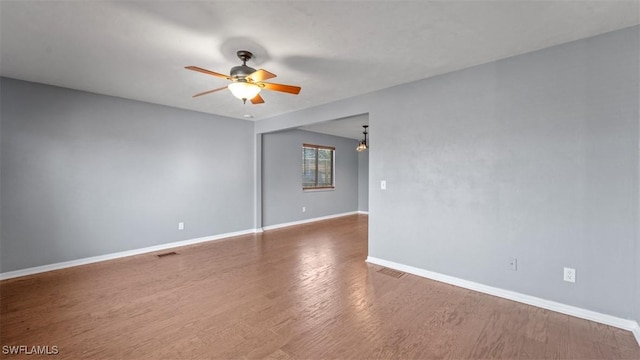 unfurnished room featuring a ceiling fan, visible vents, baseboards, and wood finished floors