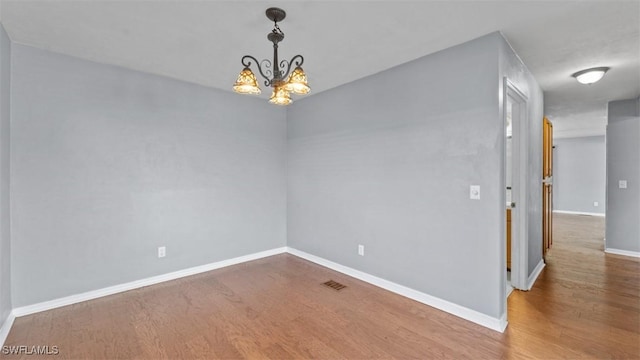 spare room with an inviting chandelier, wood finished floors, and baseboards