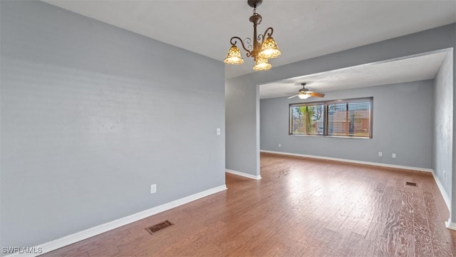 spare room with ceiling fan with notable chandelier, wood finished floors, visible vents, and baseboards