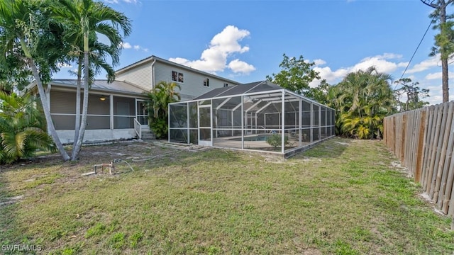 back of house with metal roof, a lawn, a fenced backyard, and glass enclosure