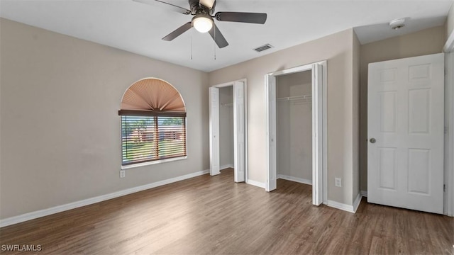 unfurnished bedroom with visible vents, baseboards, ceiling fan, wood finished floors, and two closets