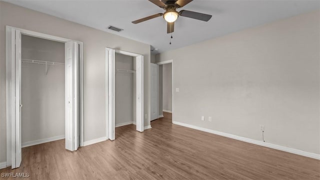 unfurnished bedroom with multiple closets, visible vents, ceiling fan, wood finished floors, and baseboards