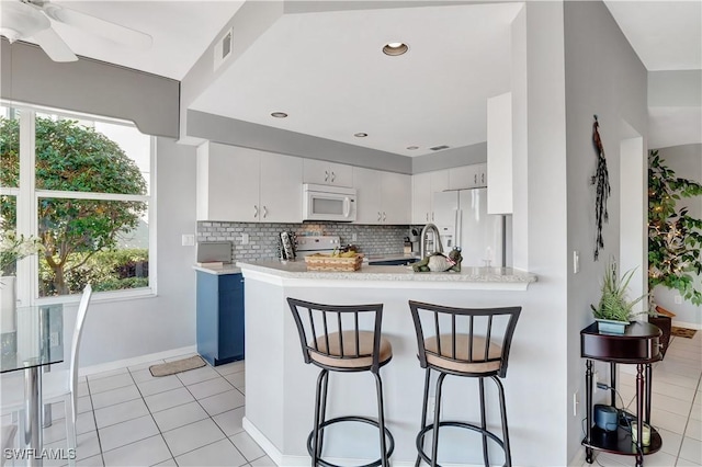 kitchen featuring white cabinetry, a kitchen breakfast bar, decorative backsplash, kitchen peninsula, and white appliances