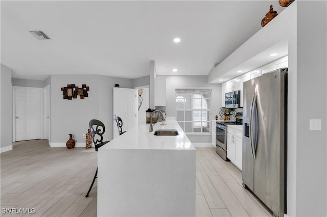 kitchen featuring sink, a breakfast bar area, appliances with stainless steel finishes, white cabinets, and kitchen peninsula